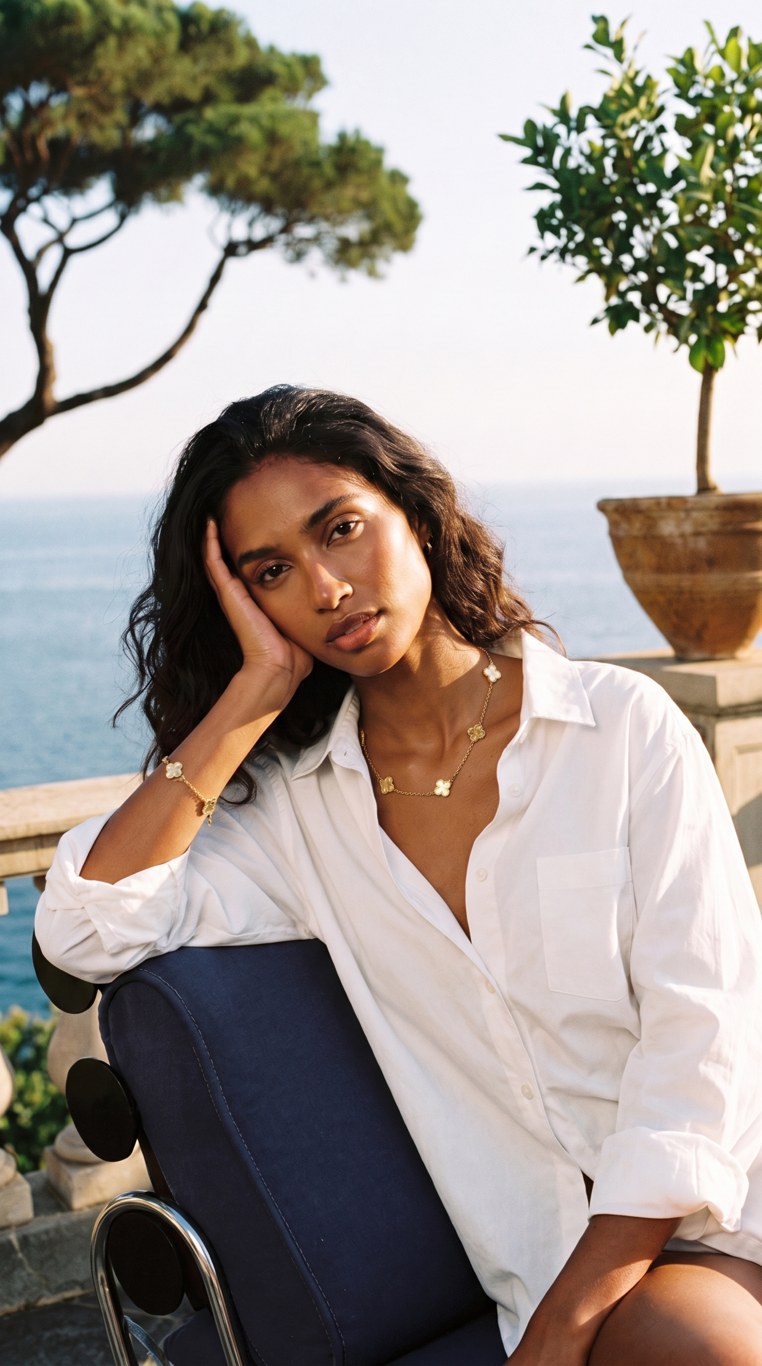 Donna sulla terrazza della Riviera italiana al tramonto indossa collana e bracciale Quadrifoglio in acciaio 316L placcato oro 18kt — Aura Gioielli
